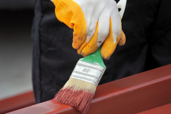 Worker painting  steel tube with paint brush selective focus on hand